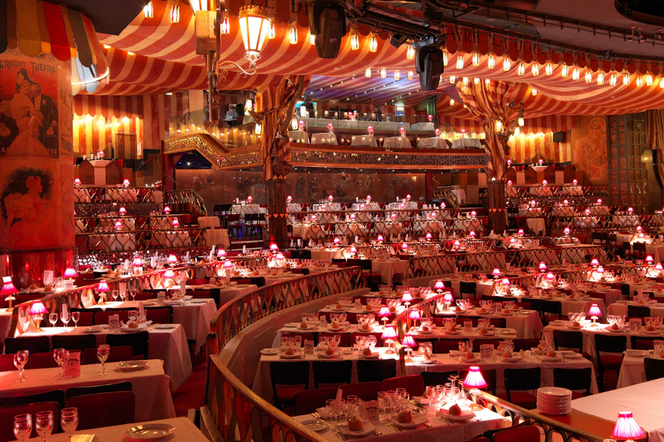 A lavishly decorated venue with multiple dining tables, red lighting, and ornate decor under a striped ceiling.