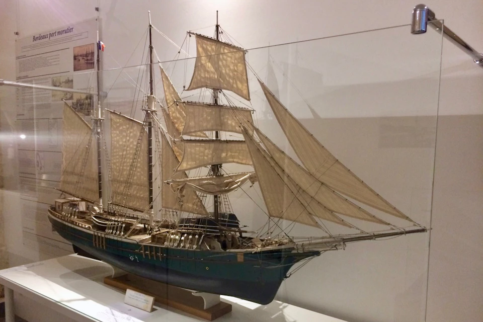 A detailed model of a sailing ship with multiple masts and sails, displayed in a museum setting on a white base.