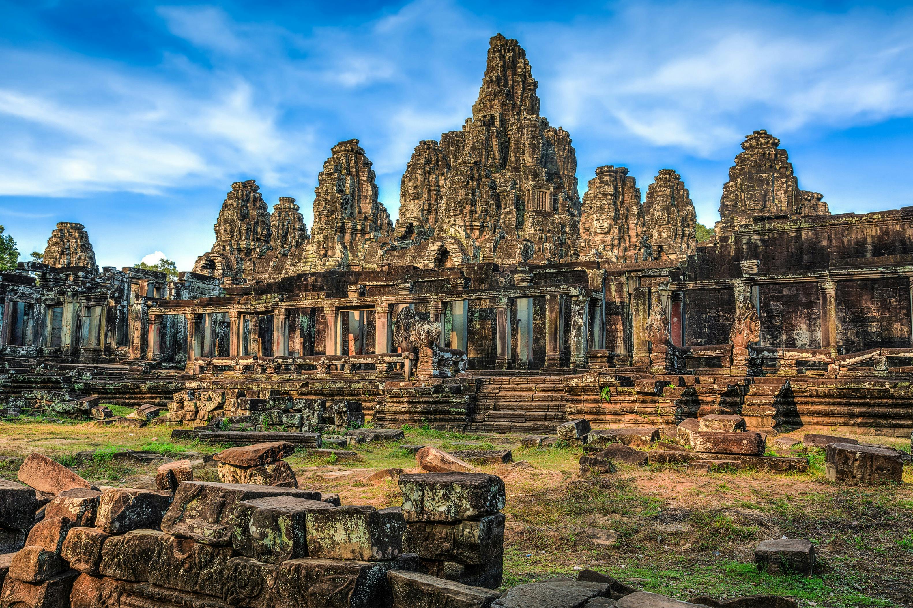 Ancient stone temple ruins with detailed carvings and multiple towers, set against a blue sky with scattered clouds.