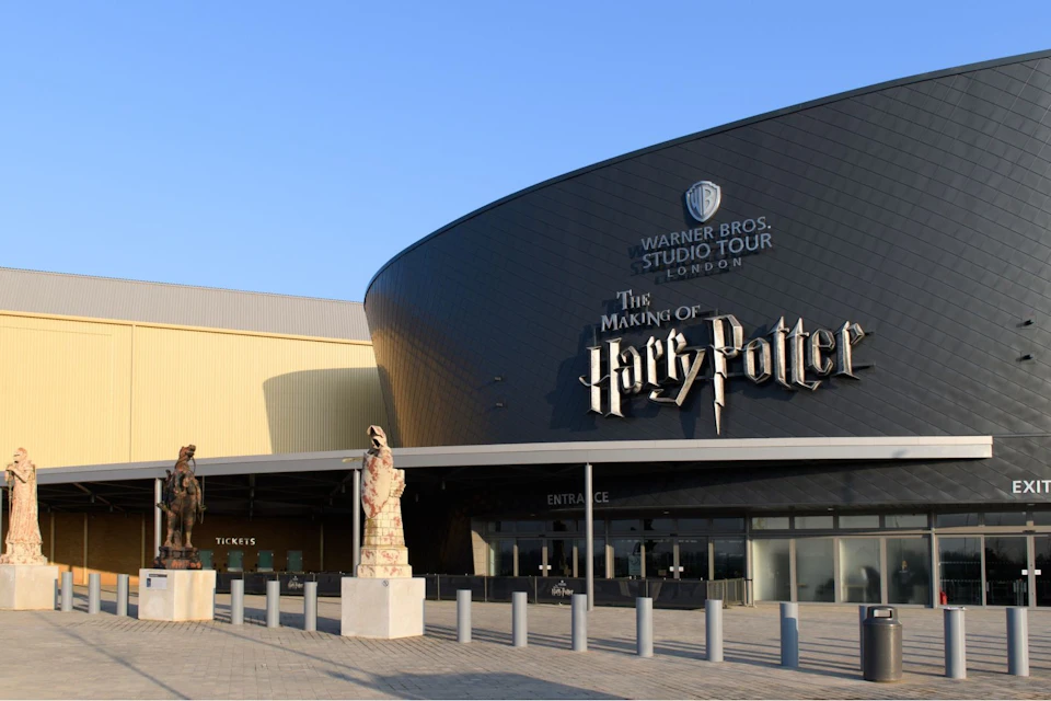 The entrance to the Warner Bros. Studio Tour in London, featuring signs for 'The Making of Harry Potter' and sculptures outside.