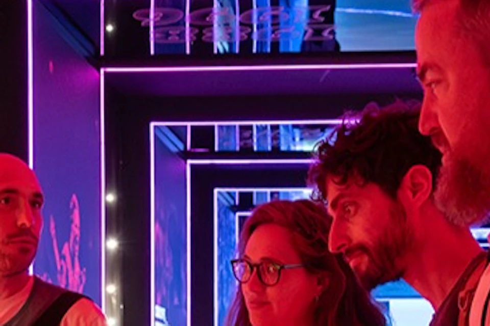 A group of four people interact in a dimly lit exhibit with vibrant red and purple lighting and informational panels.