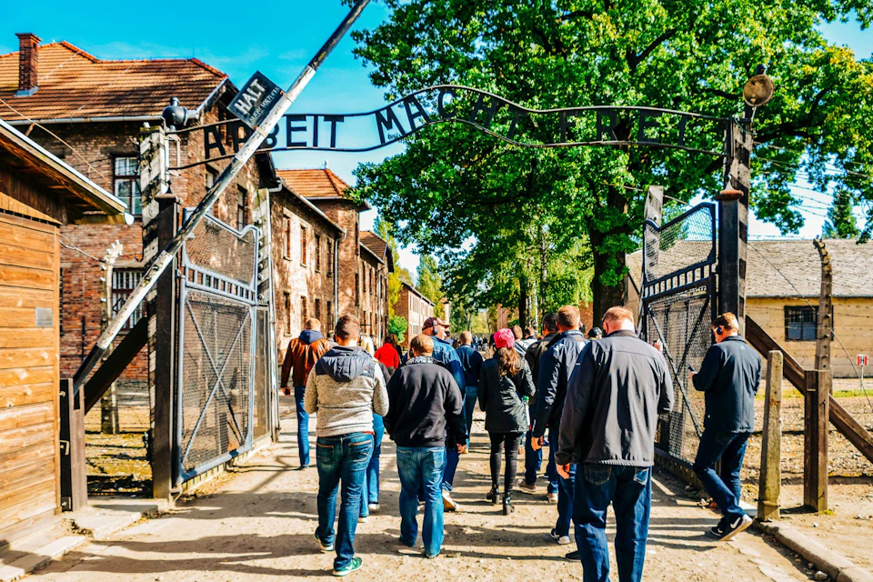 A group of people walking through the gates of a historic site with the inscription "Arbeit macht frei."