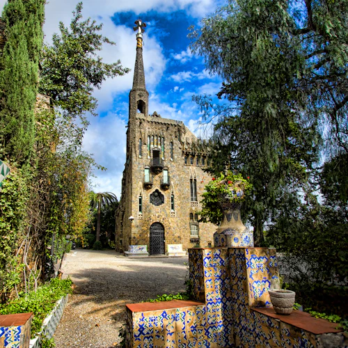 En historisk stenbyggnad med en hög spiral, omgiven av träd och invecklat blått och gult kakelarbete i förgrunden.