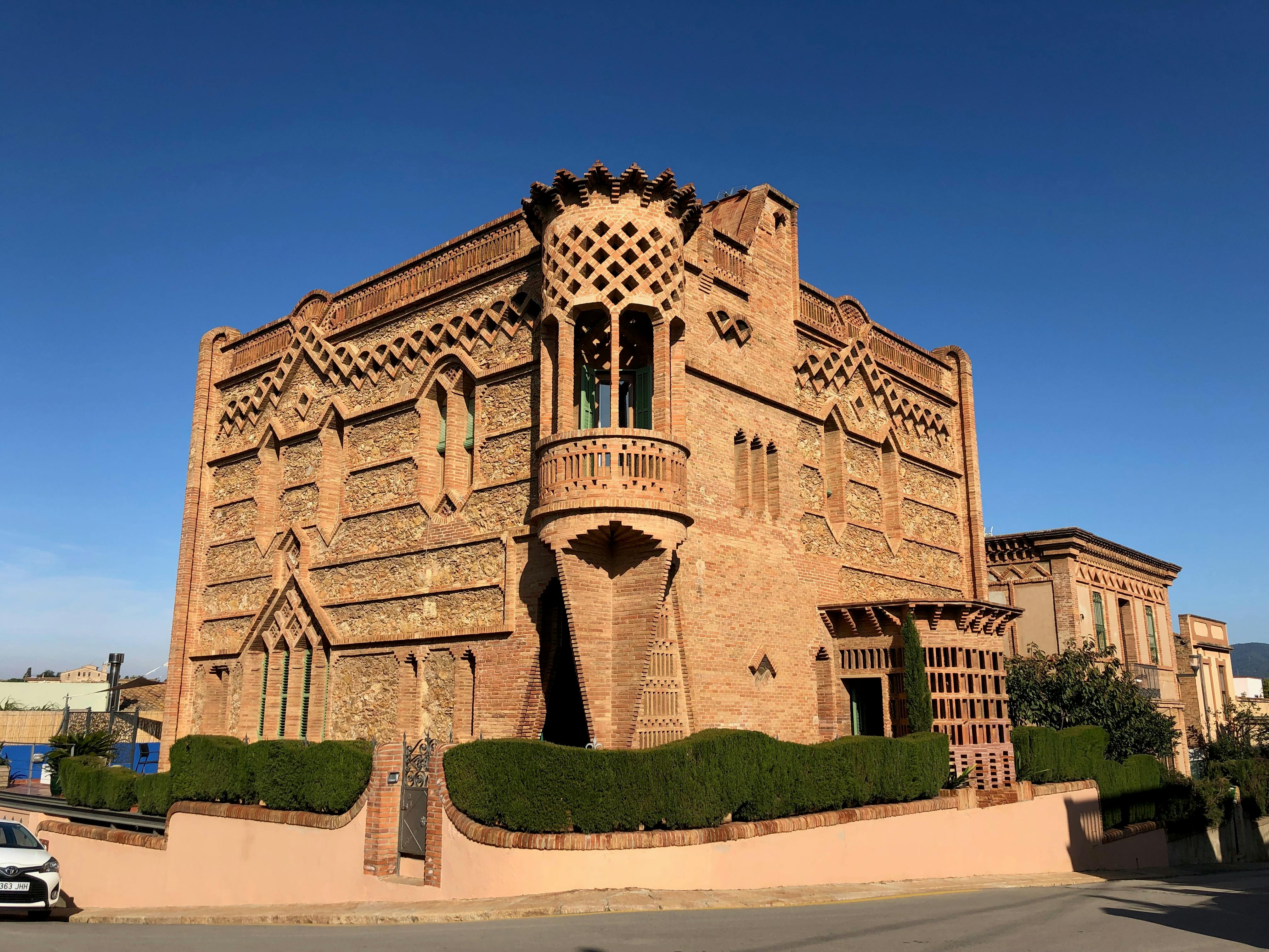 Ornate, multi-story brick building with intricate geometric patterns and a small balcony under a clear blue sky.