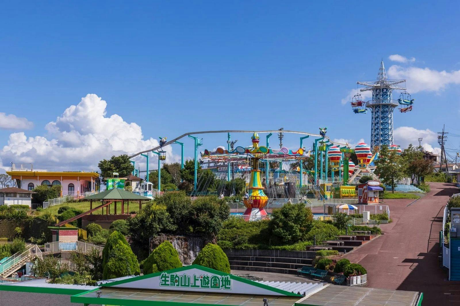 다채로운 놀이기구, 녹색 조경, 맑고 푸른 하늘이 있는 놀이공원. 한자가 있는 간판이 전경에 보입니다.