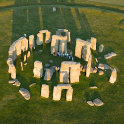 Flygfoto över Stonehenge med stora stenar som bildar en cirkel på ett gräsbevuxet fält, med människor som står inuti formationen.