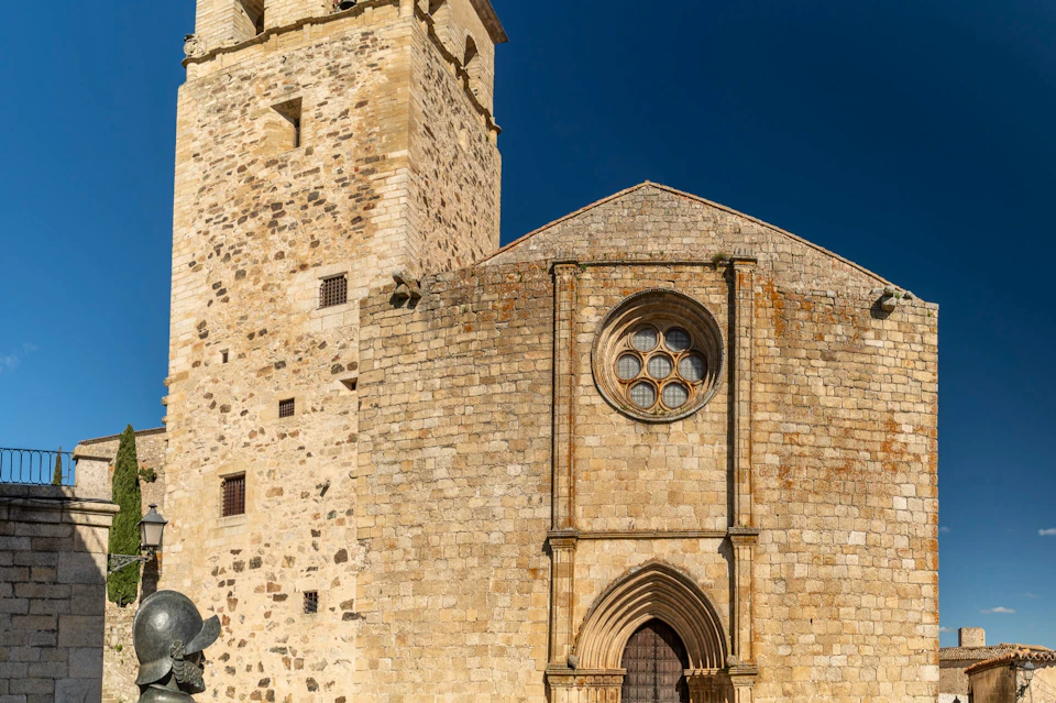 A stone building with a tower and a facade featuring a circular window and an arched doorway under a clear blue sky.