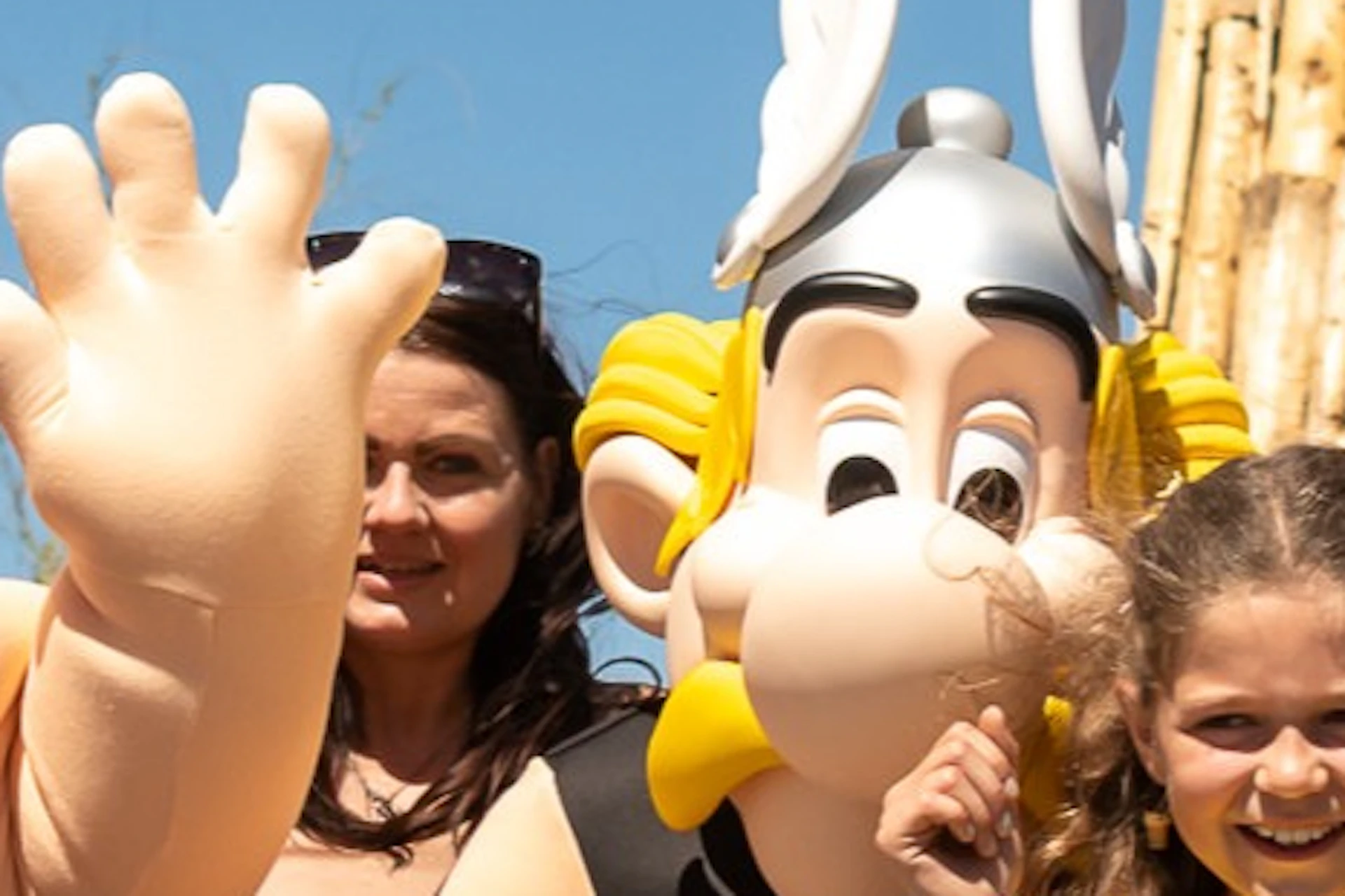 A group of people posing with costumed characters in front of a sign reading 'Idéfix Abenteuerland' and a themed building.