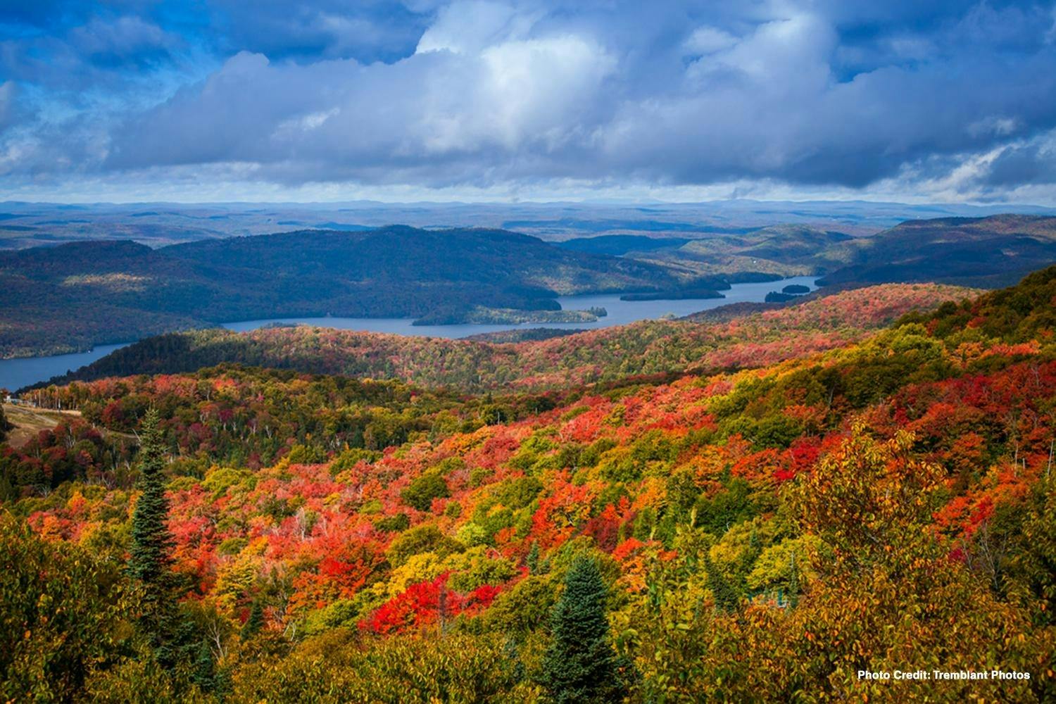 连绵起伏的山丘和湖泊，周围环绕着部分多云的天空下生机勃勃的秋叶。