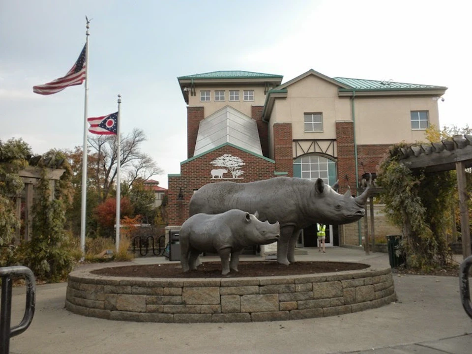 Statues of two rhinoceroses on a stone platform, with a building and two flags in the background.