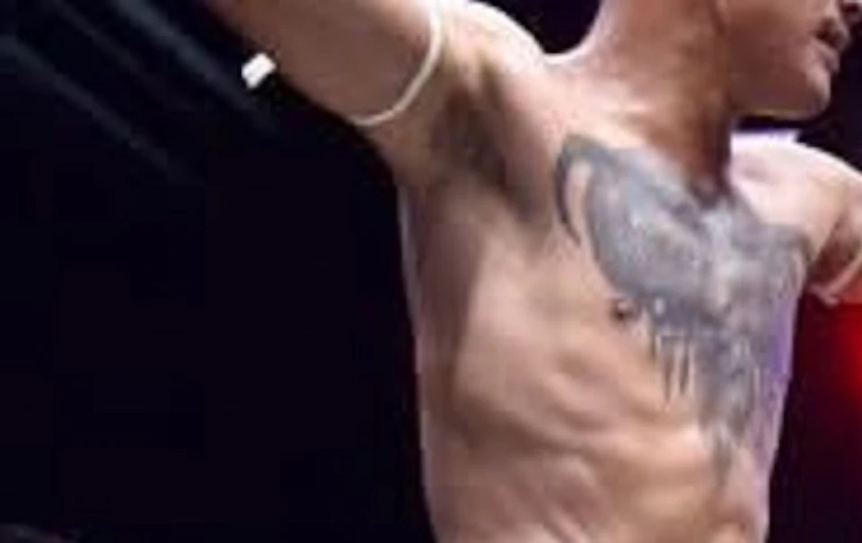 A Muay Thai fighter celebrates in a ring after a match. A defeated opponent lies on the ground. A scoreboard is visible.
