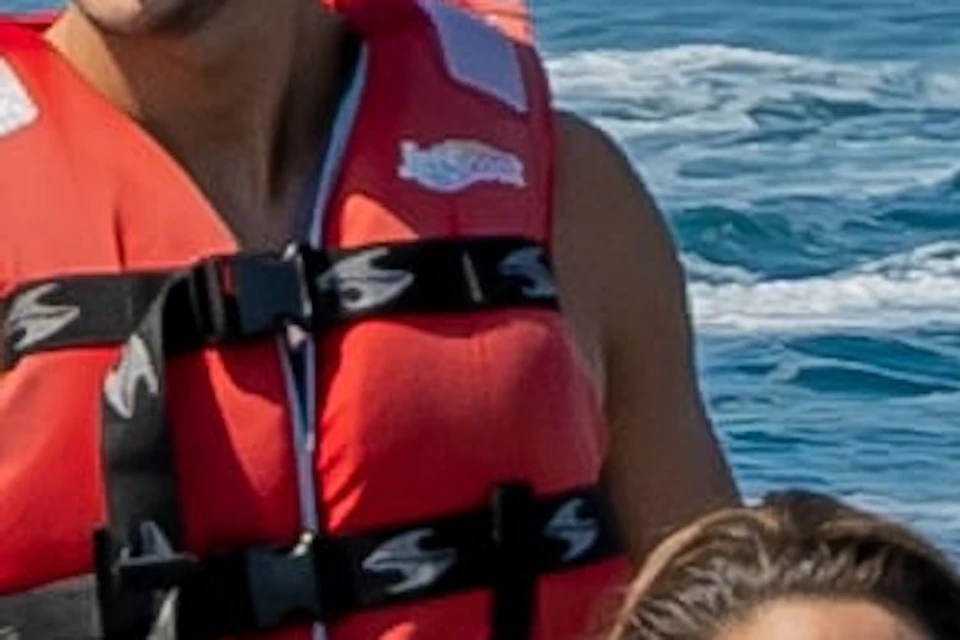 People on jet skis ride in the ocean near a city shoreline with a distinctive curved building and other structures in the background.