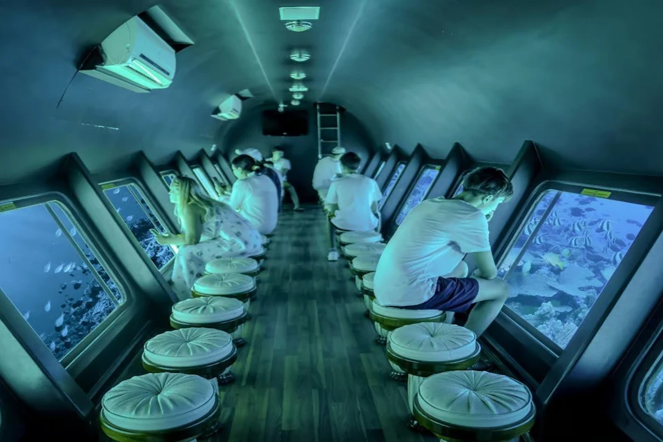 People sitting inside a submarine, viewing underwater scenes through window panels along the sides.