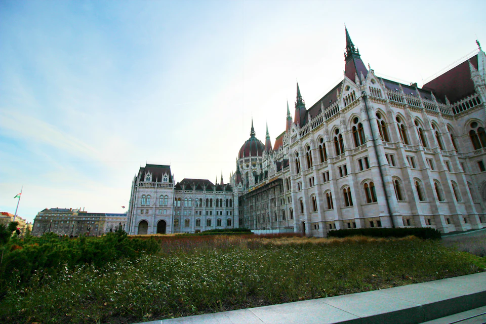 Large, ornate building with pointed spires and dome, set against a clear sky; grass and small bushes in the foreground.