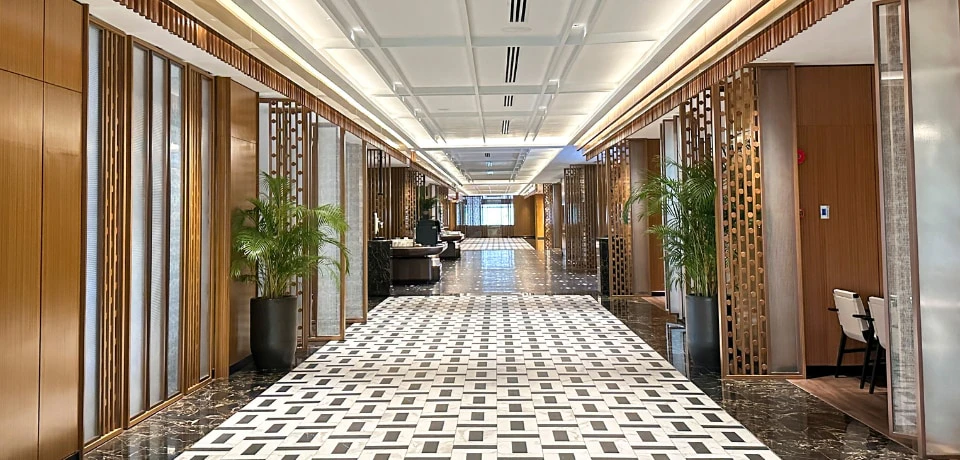 A modern, elegant hotel lobby with patterned flooring, potted plants, decorative wooden panels, and a reception desk.