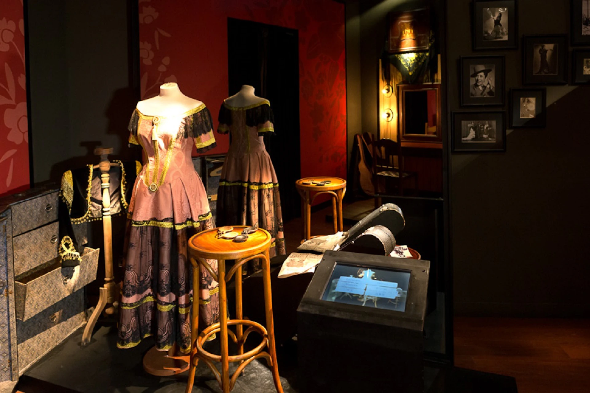 Mannequins dressed in vintage clothing, stools, a hat, a guitar, framed photos, and a display case in a dimly lit room.