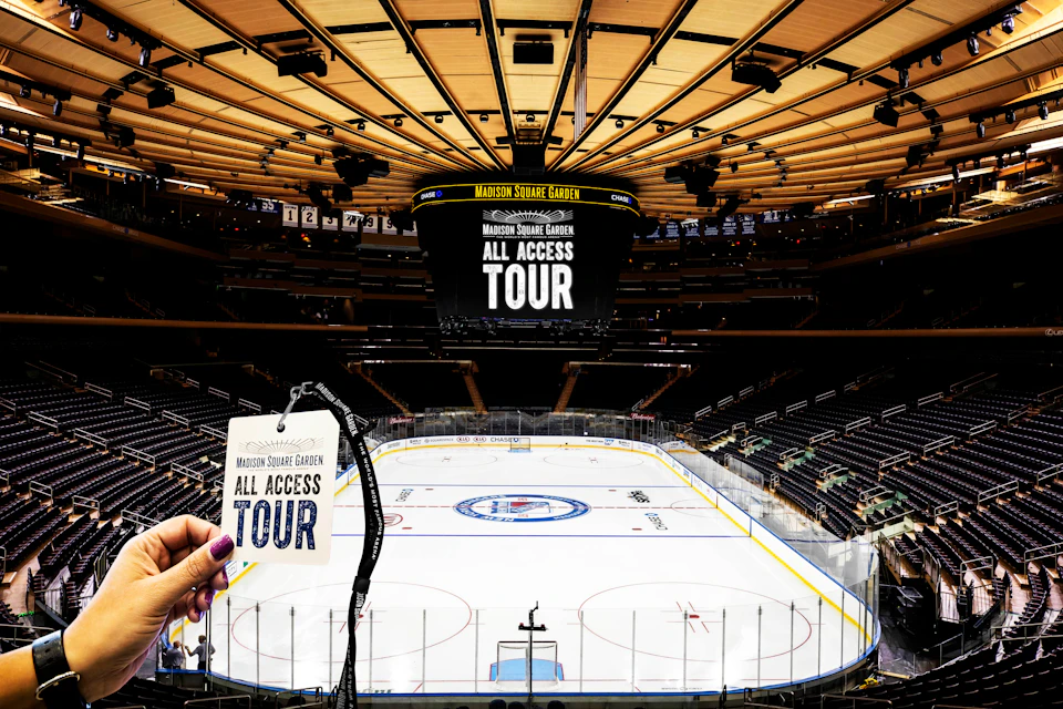 Empty indoor hockey rink with "Madison Square Garden All Access Tour" on the scoreboard and a hand holding a tour pass.