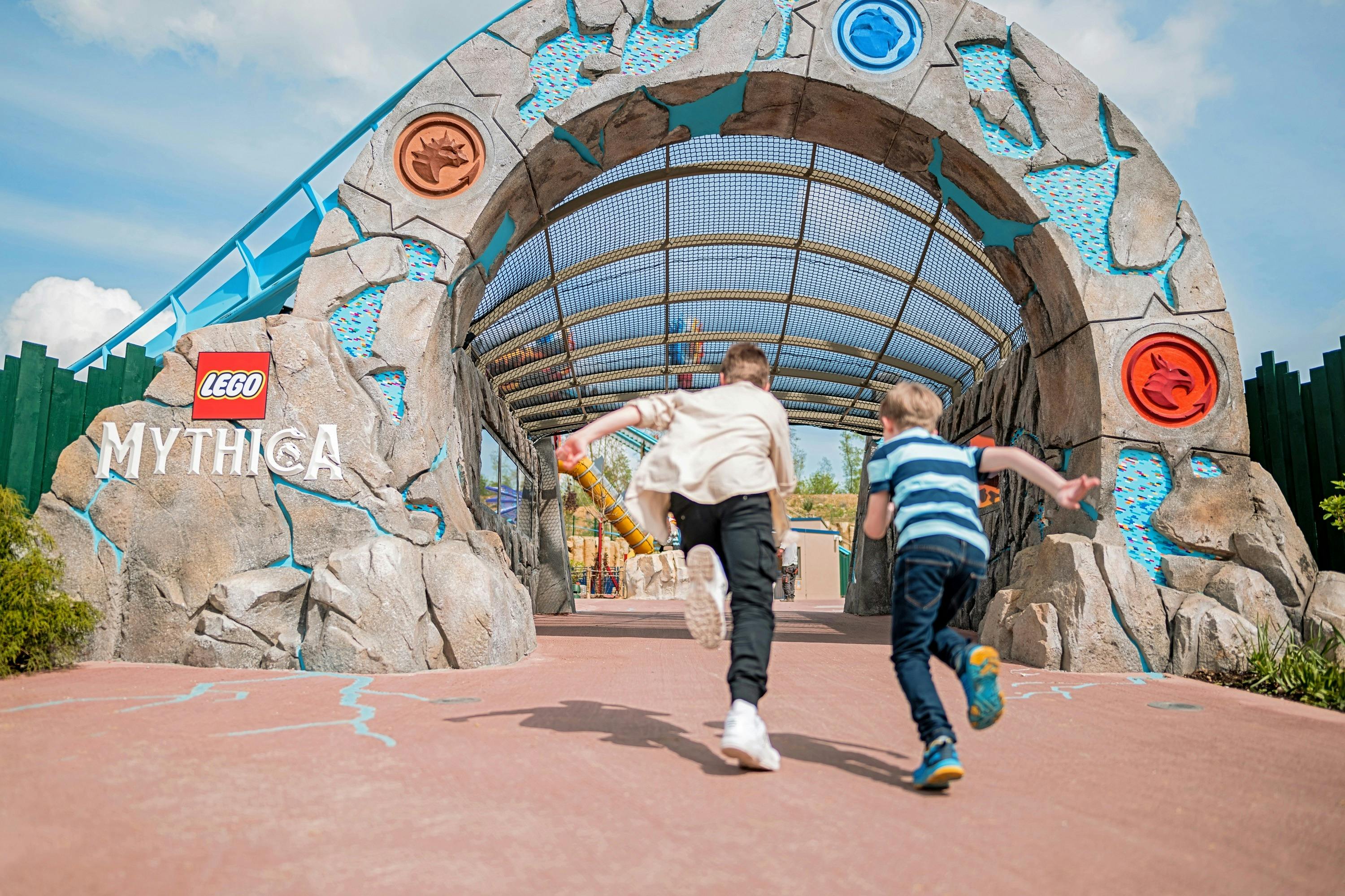 Two children running towards a themed archway with decorations, labeled "Lego Chima," under a sunny sky.