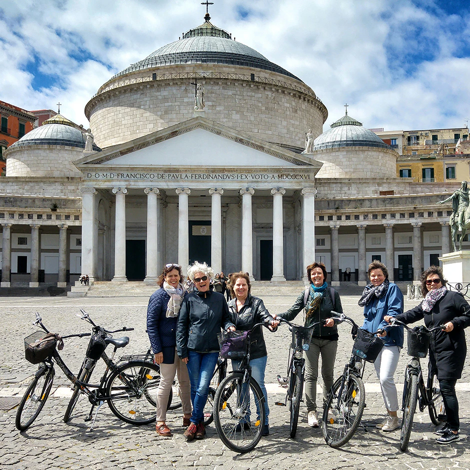 Six people standing with bicycles in front of a large, domed building with columns and a cross on top.