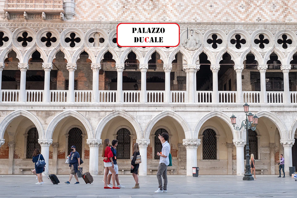 Five people walking near a historic white building with arches and a sign that reads "Palazzo Ducale."