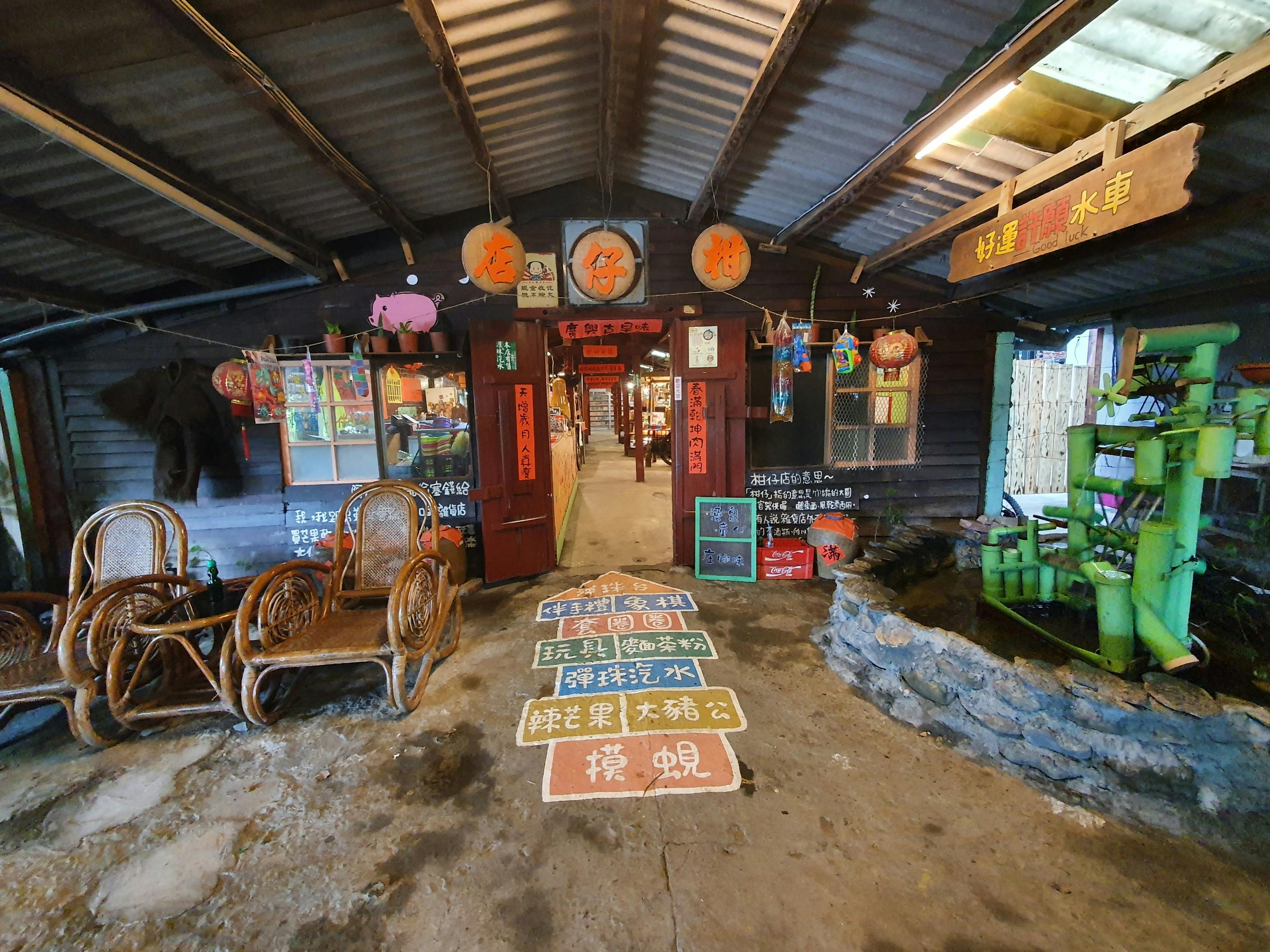 A decorated shop entrance with lanterns, signs with Chinese text, wicker chairs, and colorful interior visible through the door.