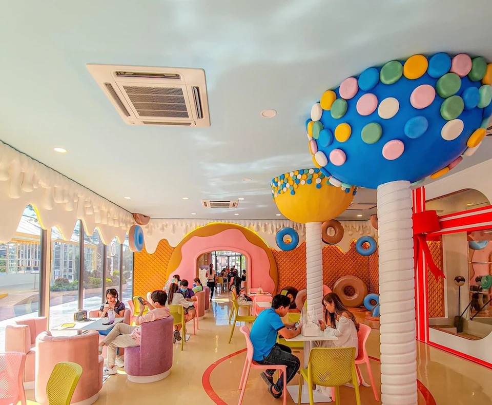 A colorful, candy-themed café with whimsical decorations, including large mushroom structures, and customers seated at tables.