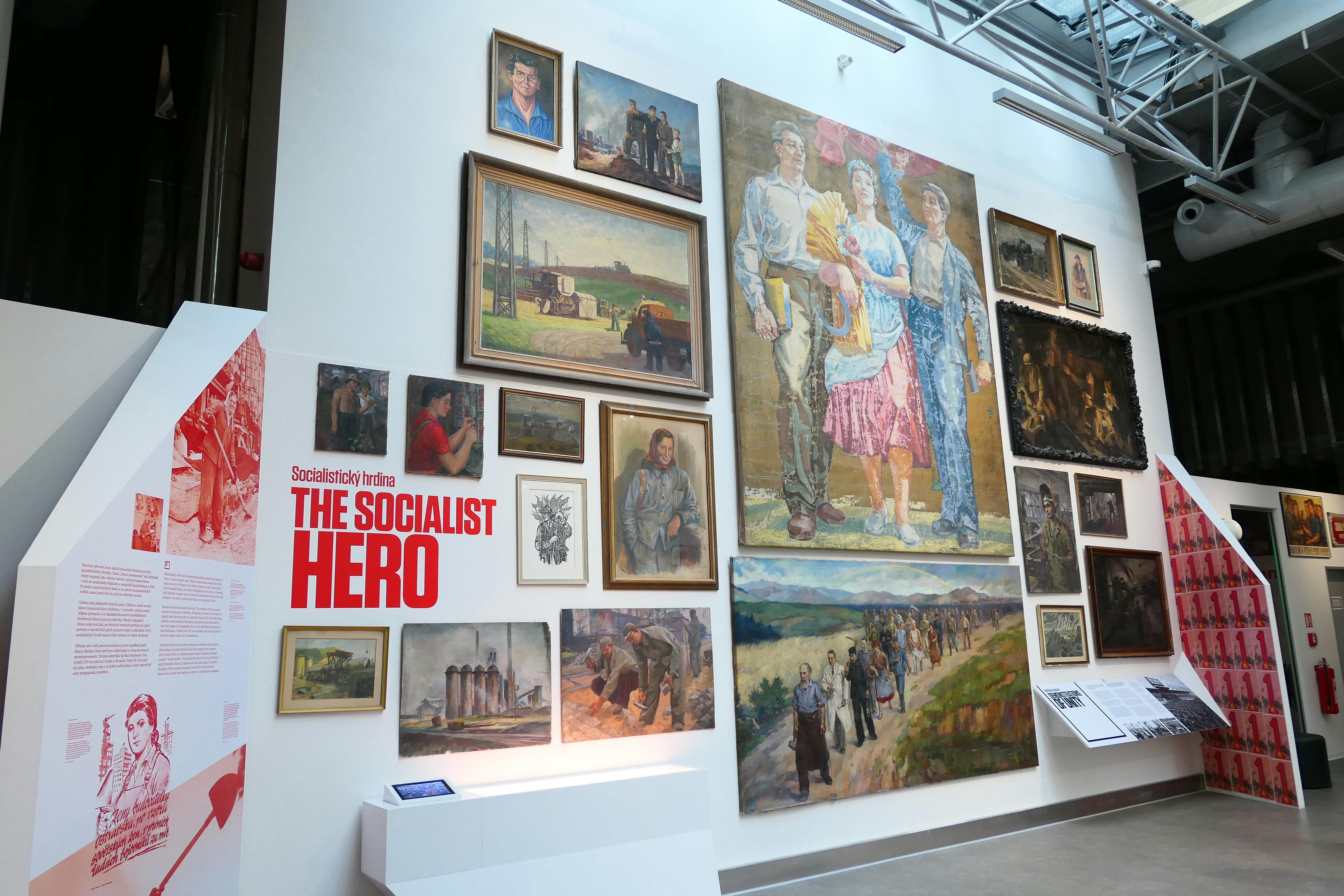 墙上展示了多幅以社会主义为主题的绘画作品，包括农村景观和工业场景中的人物，标有“社会主义英雄”。