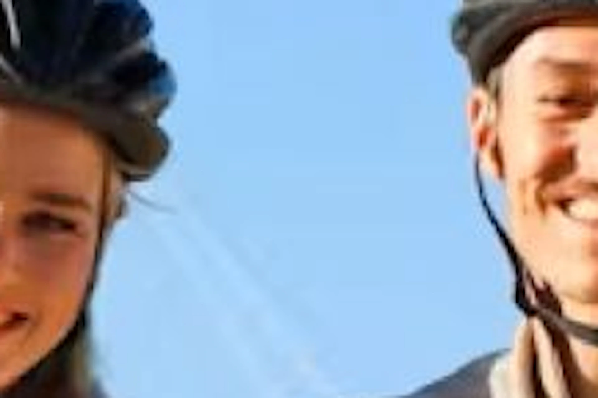Two people with bicycles standing near a waterfront with a ship in the background on a sunny day.