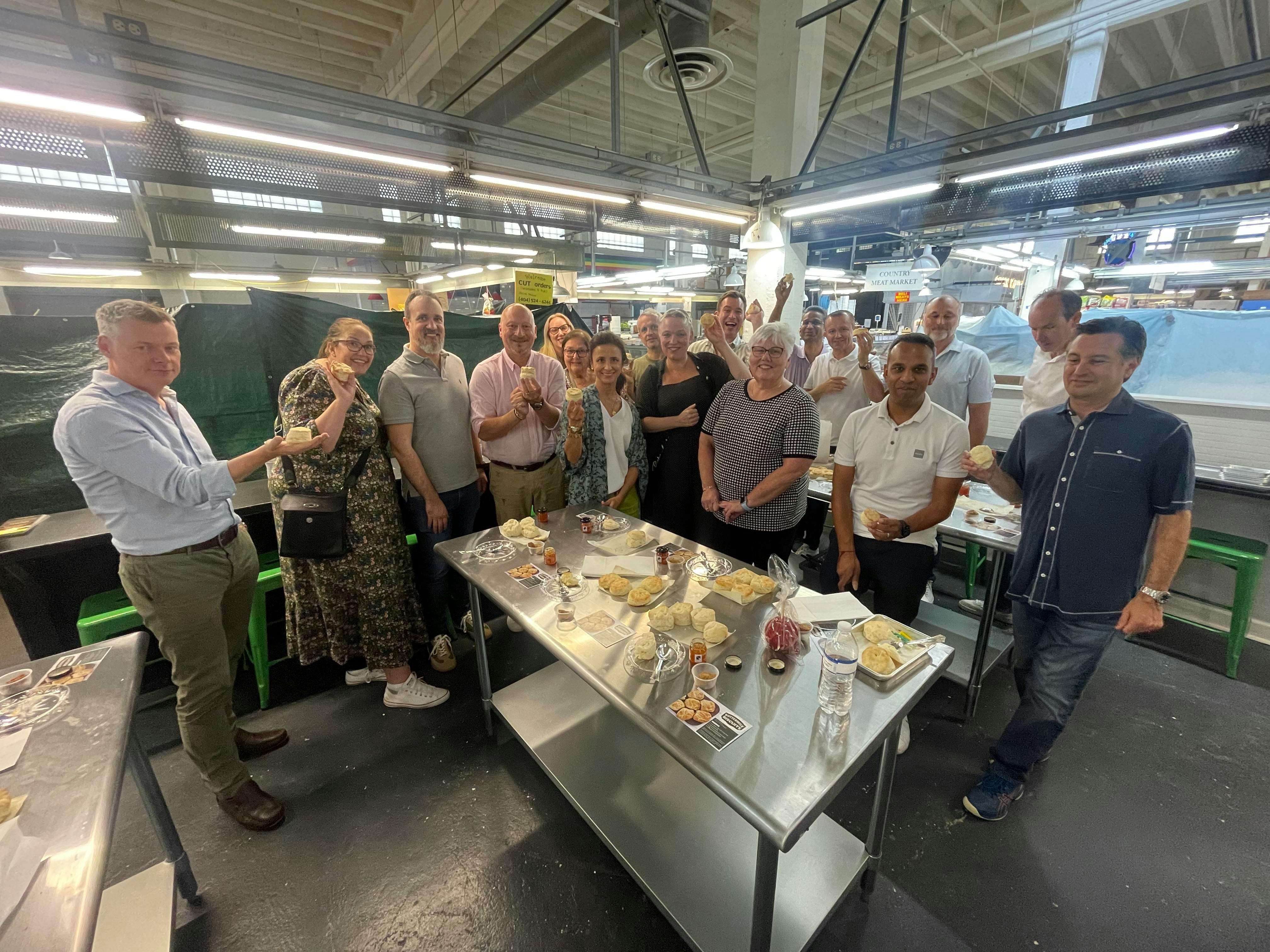 인더스트리얼한 분위기의 다양한 음식이 놓인 금속 테이블 주위에 서 있는 사람들의 모임.