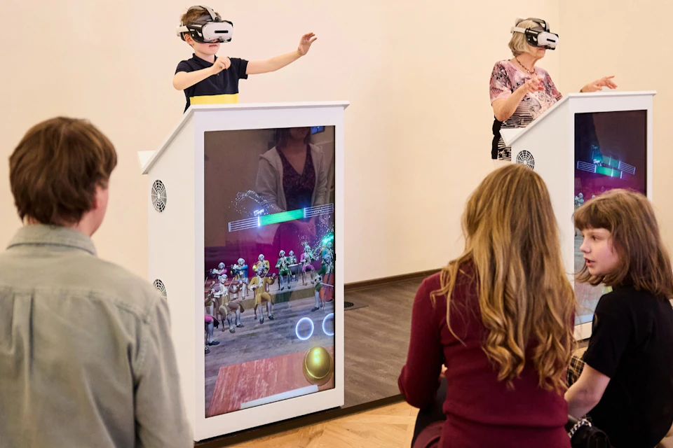 People interacting with virtual reality displays; two wearing VR headsets, two seated observing the interactive screens.
