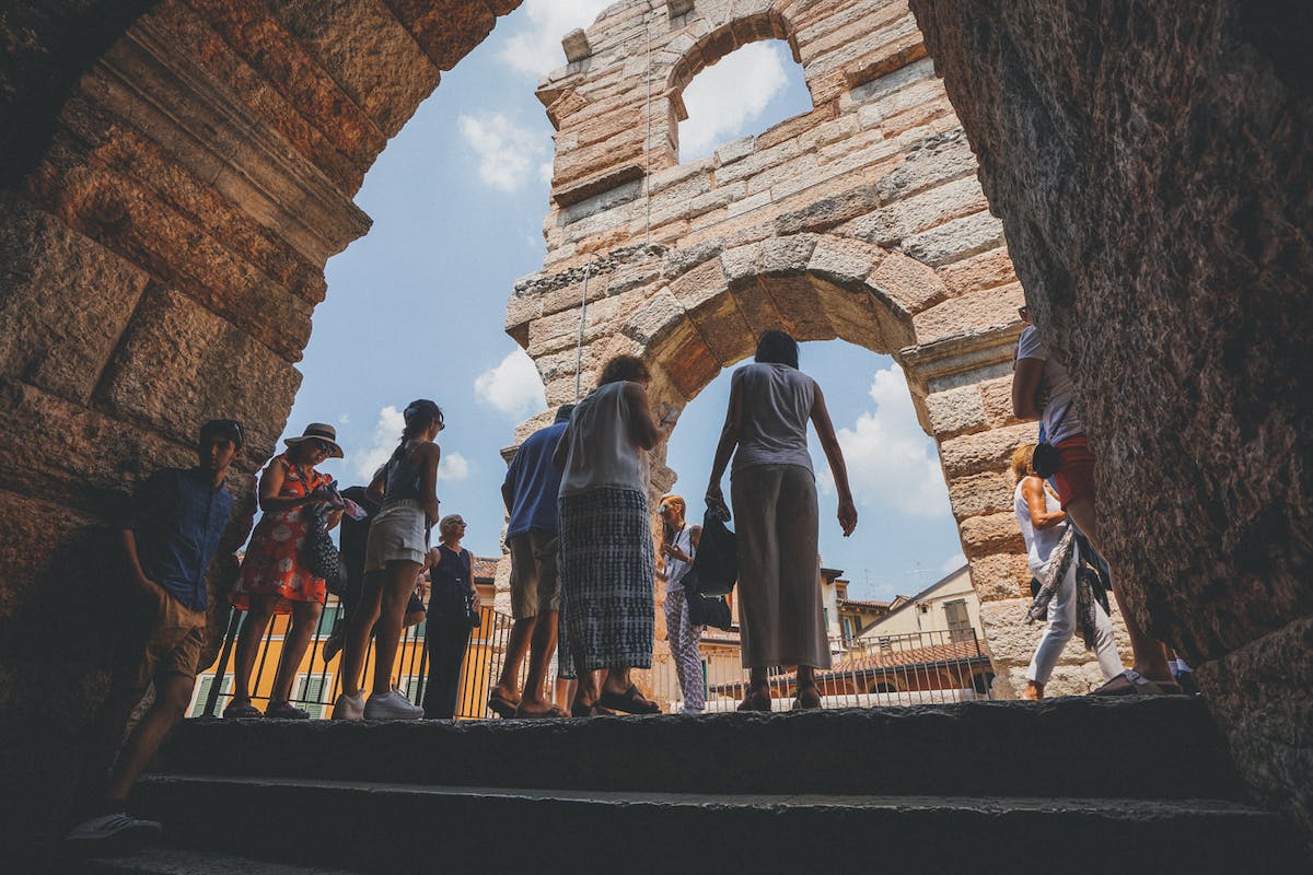 People standing and walking near ancient stone arches against a bright blue sky.