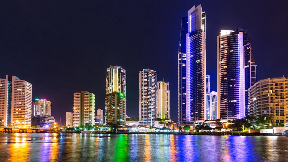 City skyline at night with illuminated skyscrapers reflecting vibrant lights on the water below.