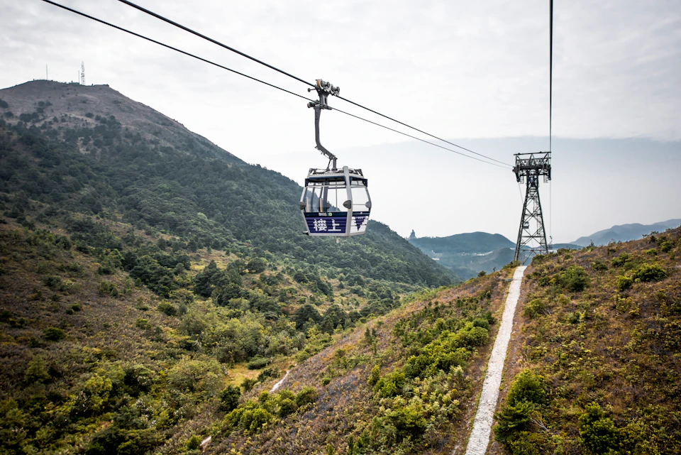 A cable car travels over a lush, mountainous landscape with misty skies above.