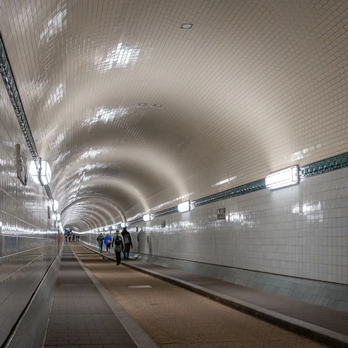 En väl upplyst kaklad tunnel med människor som går längs en central stig, upplyst av ljus på väggarna.