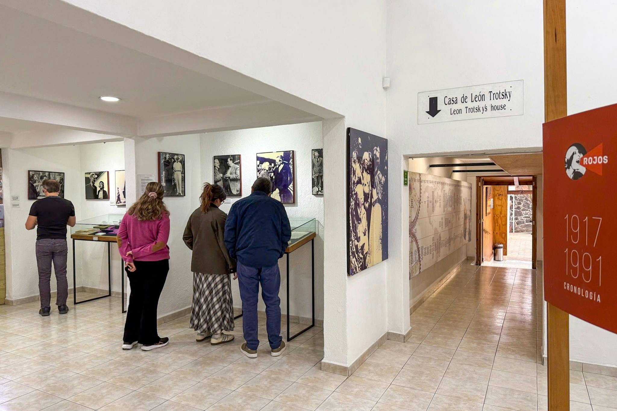 Tre personer, der undersøger udstillinger på et museum med etiketten 'Casa de León Trotsky.'Vægge viser billeder og historiske oplysninger.