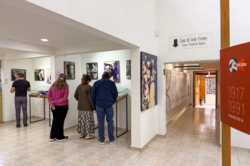 Three people examining exhibits in a museum with labeled 'Casa de León Trotsky.' Walls display photos and historical information.