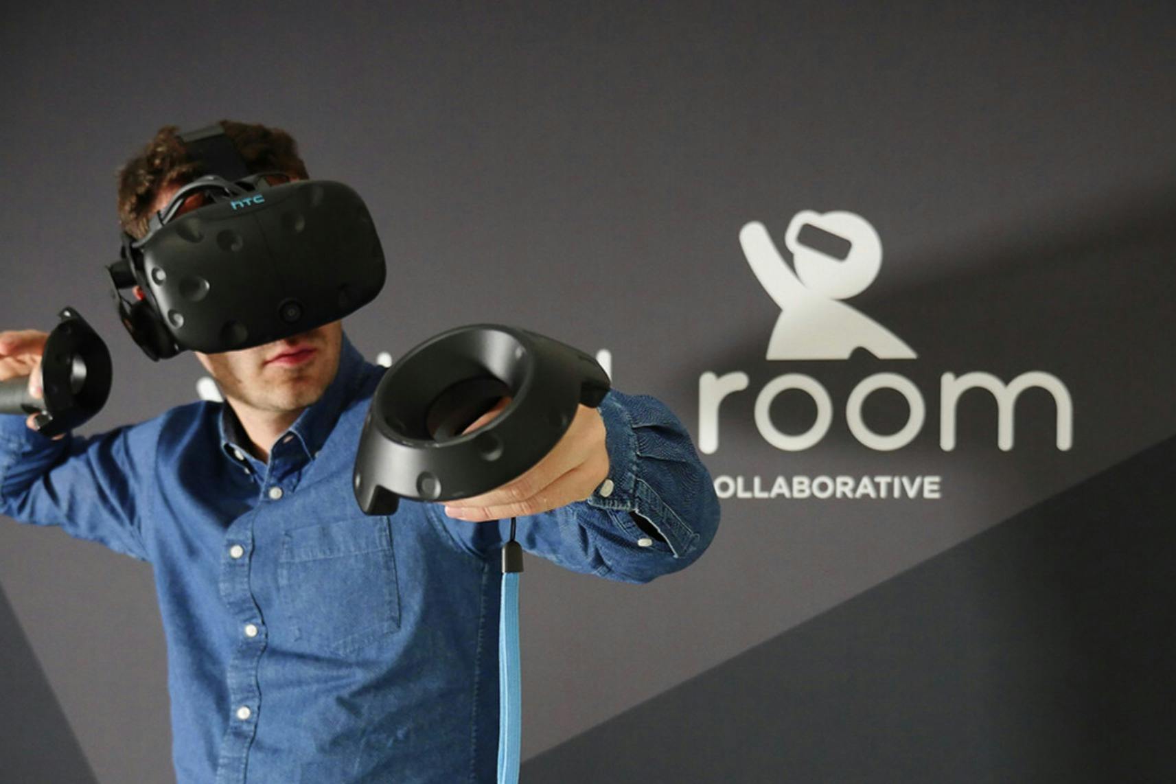 Uma pessoa com um auricular de realidade virtual e comandos de movimento numa sala com um fundo escuro e texto visível na parede.