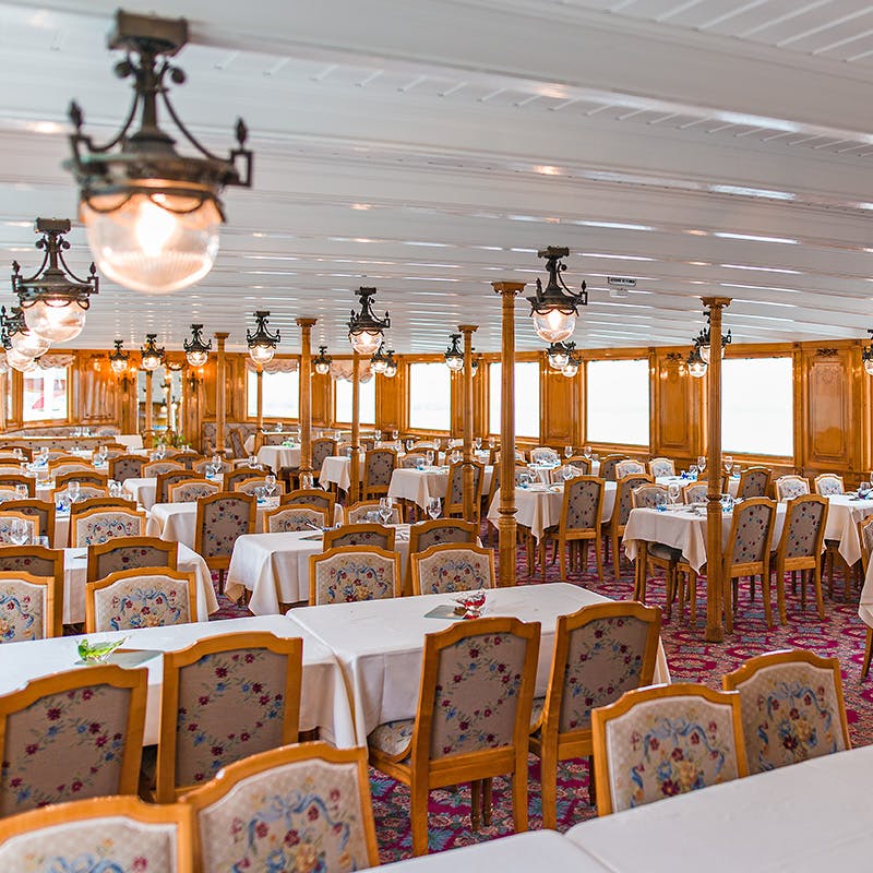 明亮华丽的餐厅，配有花卉图案椅子、白色桌布和复古吊灯。