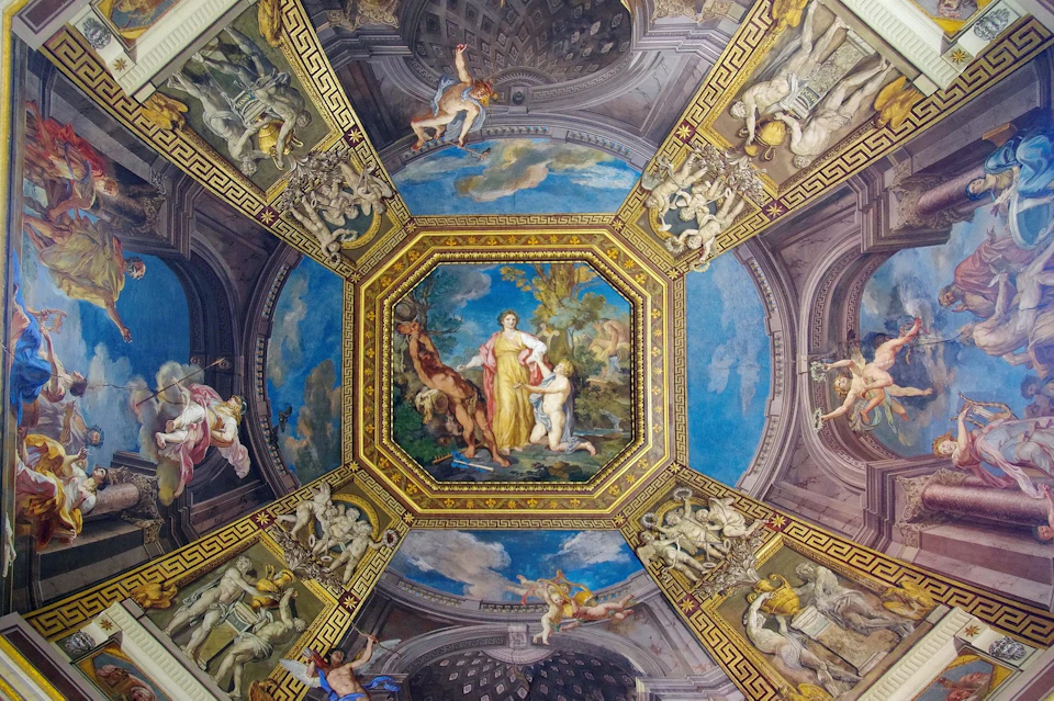 A highly ornate ceiling with a central painting of figures and surrounding panels depicting mythological scenes in rich colors.