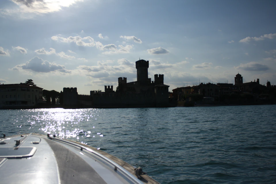 Silhouette of a castle with towers by the water, viewed from a boat, under a partly cloudy sky.