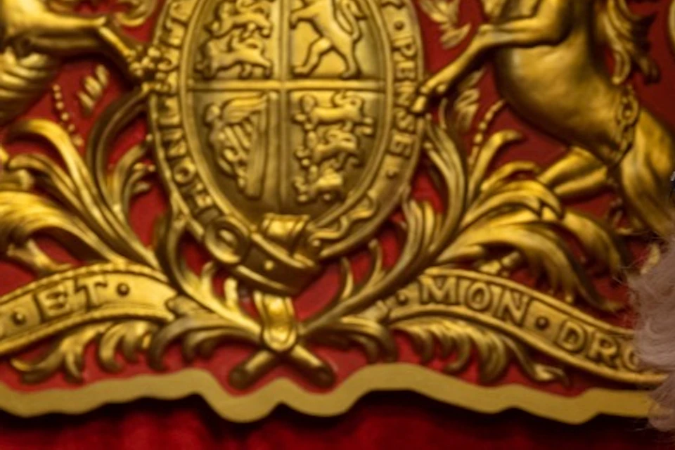 A man and a woman in formal attire stand in front of a red and gold ornate backdrop with two red and gold chairs.