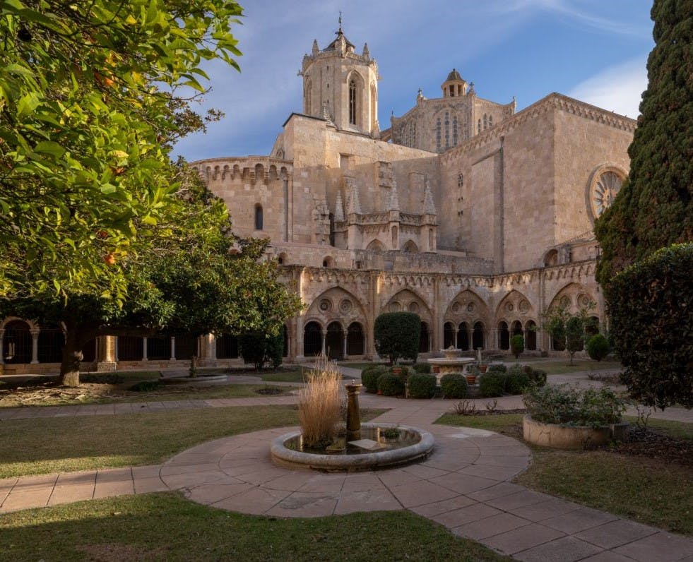 这座历史悠久的石头大教堂设有拱形修道院，周围环绕着修剪整齐的花园和蓝天下的中央喷泉。