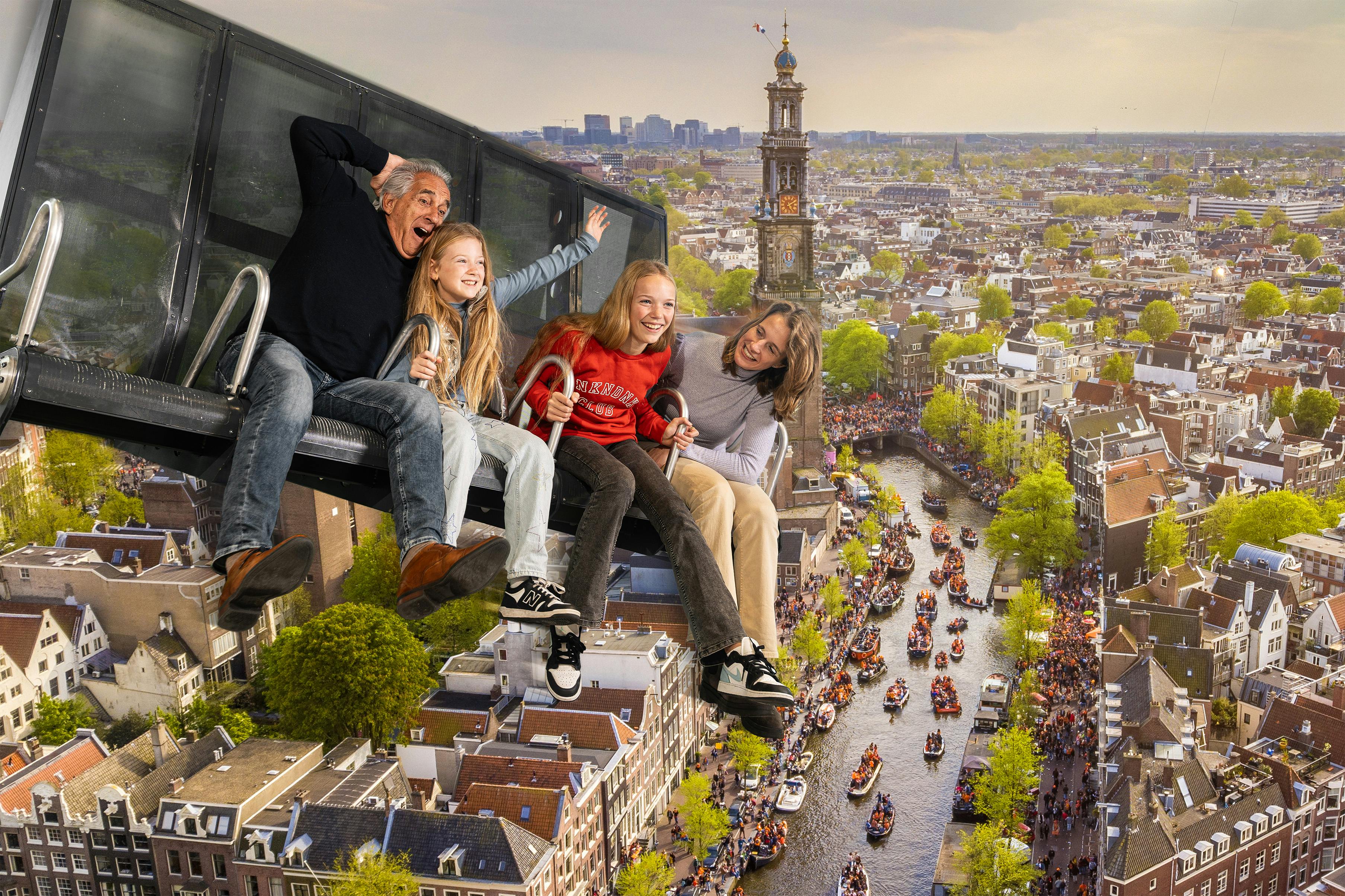 Vier mensen zitten in een attractie boven een Europese stad met grachten en een prominente kerktoren op de achtergrond.