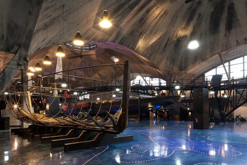 Interior of a museum featuring an old wooden ship frame on display, with dim lighting and a large, curved ceiling.