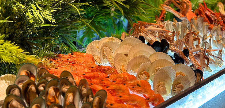 An assortment of seafood including shrimp, scallops, and mussels displayed on ice with decorative greenery.