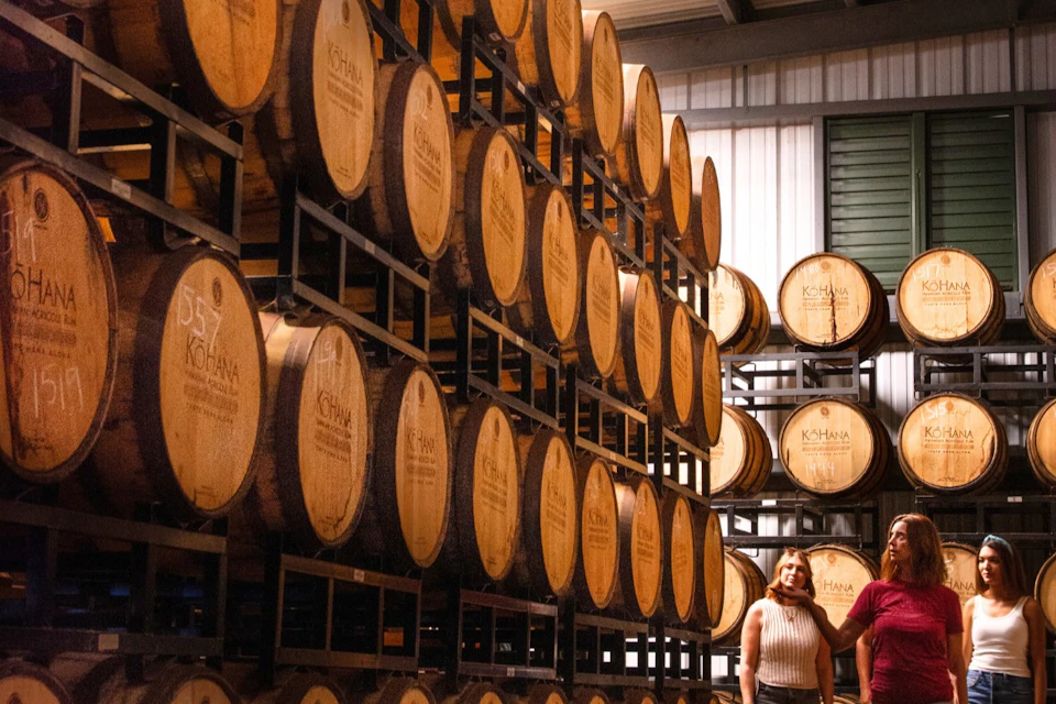 A warehouse interior with stacked wooden barrels, labeled Kohana, and a woman standing near the bottom right corner.
