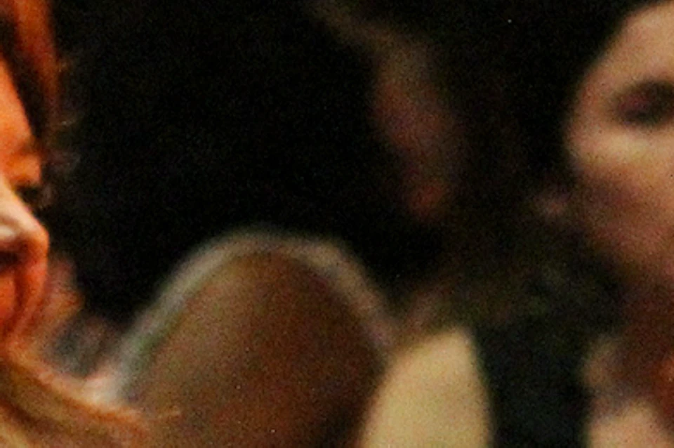 People sitting at a small table with drinks and snacks, smiling and chatting in a dimly lit setting.