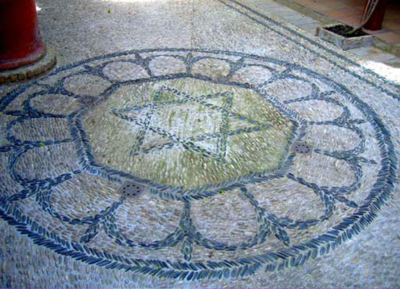 Mosaico in pietra intricato con un disegno centrale a stella circondato da un motivo a petali su una superficie pavimentata.