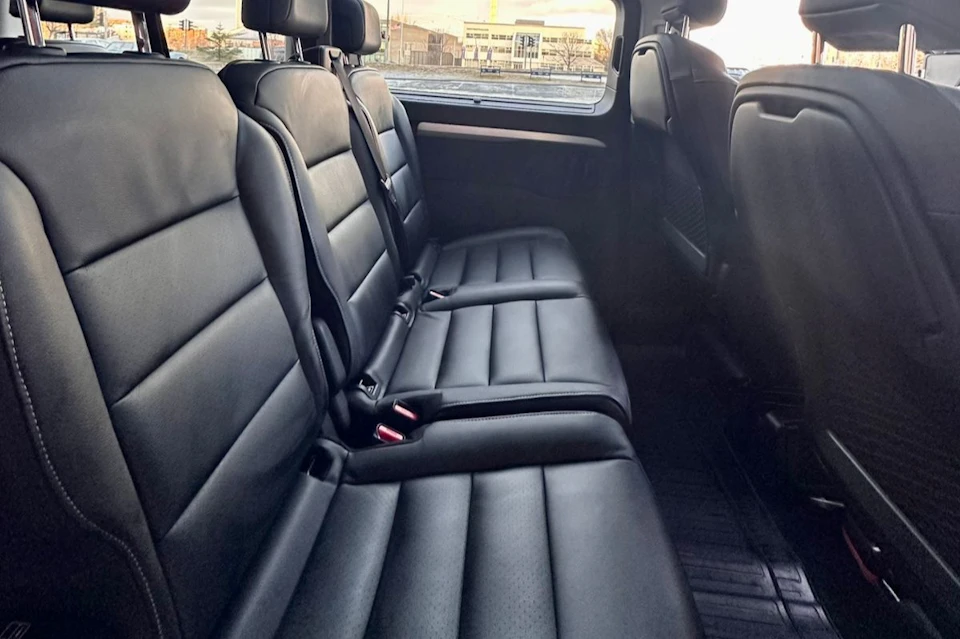 The interior of a vehicle showing black leather seats in a back row, with a view of buildings through the window.