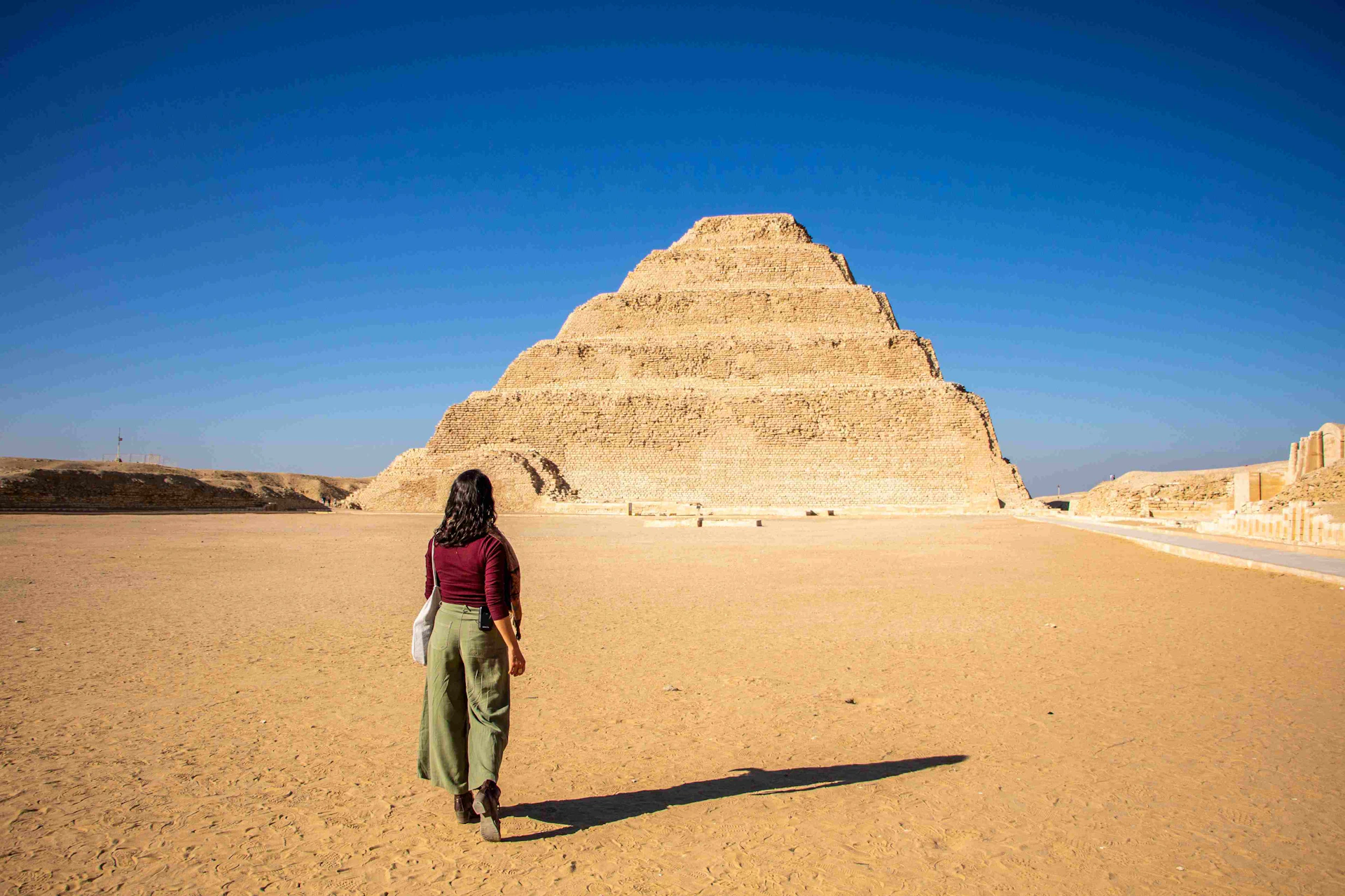 A person walking towards the Step Pyramid of Djoser under a clear blue sky in a desert setting.